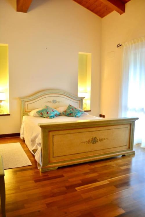 Bright bedroom at Agriturismo Colle Mura with wooden bed, cream walls, exposed beams, and hardwood floors in Gualdo Tadino