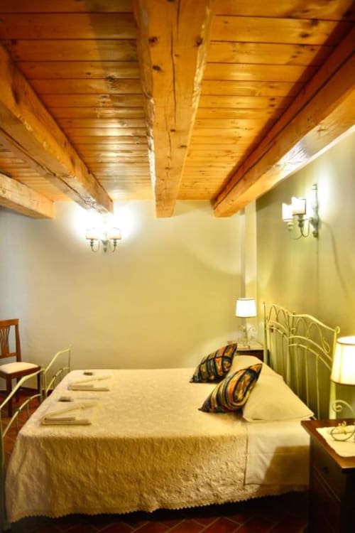 Cozy bedroom at Agriturismo Colle Mura in Gualdo Tadino with exposed wooden beams, cream bedding, and warm lighting