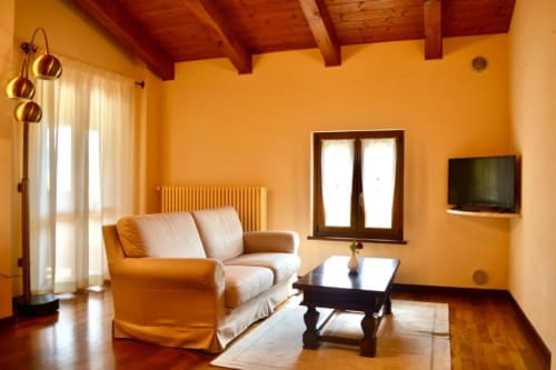 Bright yellow living room at Agriturismo Colle Mura in Gualdo Tadino with beige sofa, wooden beams, and modern amenities