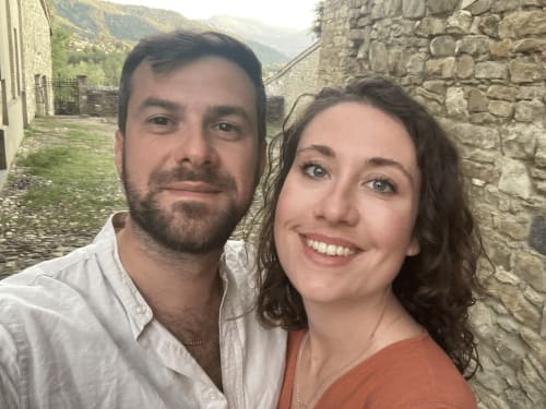 Couple smiling at Agriturismo Colle Mura in Gualdo Tadino, Italy, with stone buildings and countryside backdrop
