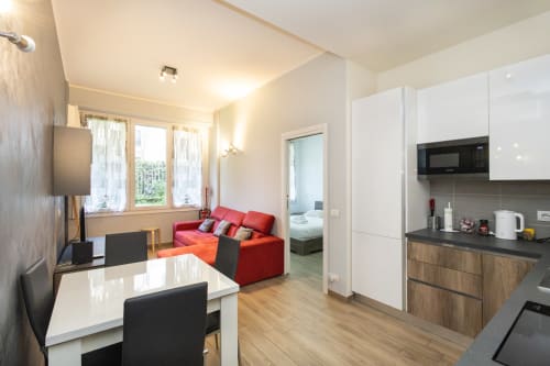 Современная квартира в Magnolia Apartments Милан с красным диваном, белой кухней, обеденным столом и видом на сад