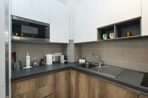 Современная кухня в апартаментах Magnolia Apartments Милан с белыми верхними шкафами, деревянными нижними шкафами и темной столешницей