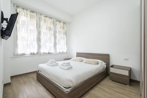 Современная спальня в отеле Magnolia Apartments Милан с деревянной кроватью, белым бельем, прозрачными шторами и паркетом