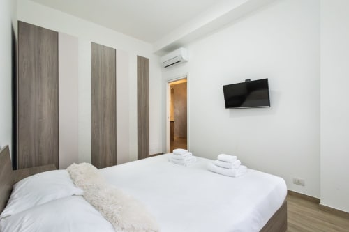 Современная спальня в апартаментах Magnolia Apartments Милан с белой кроватью, деревянным шкафом, плоским ТВ, кондиционером и теплым паркетом
