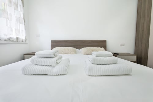 Современная спальня в отеле Magnolia Apartments Milan с аккуратно расположенными белыми полотенцами на двуспальной кровати и бежевыми подушками