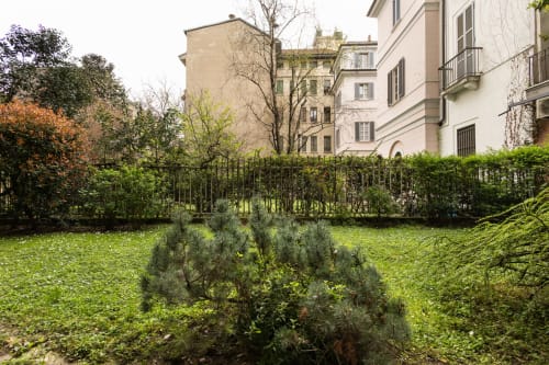 Пышный зеленый внутренний двор с оливковыми деревьями в Magnolia Apartments Milan, окруженный элегантными историческими зданиями и черным