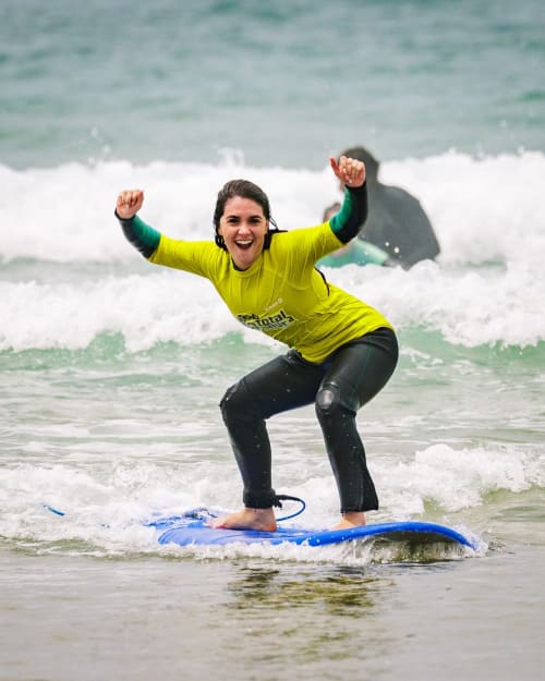 Surfista feliz em proteção amarela andando de pranchas azul na praia de Vila Alexandra, Costa da Caparica, Portugal.