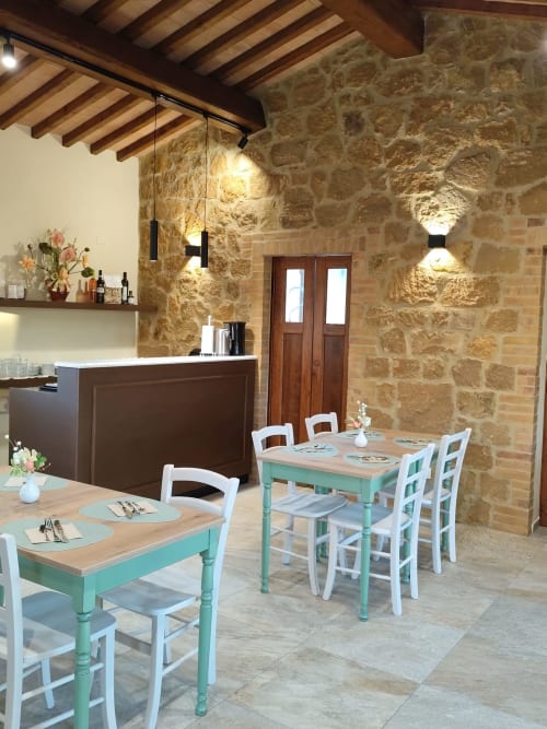 Sala da pranzo rustica dell'Agriturismo Marinello a Pienza con tavoli turchesi, muri in pietra e travi in legno