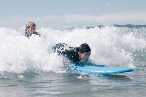 Jovem surfista a cavalgar ondas em prancha azul na praia de Vila Alexandra, Costa da Caparica Portugal