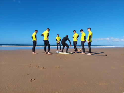 Grupo de surfistas em trajes de banho amarelos e pretos reunidos na praia de Costa da Caparica para aula pela pousada Vila Alexandra