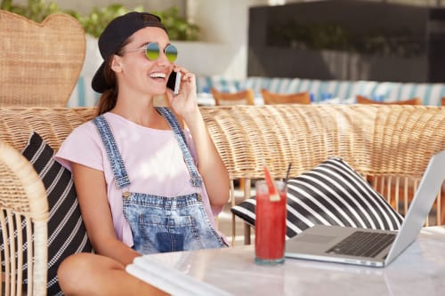 Jovem mulher ao telefone na pousada Vila Alexandra em Costa da Caparica, relaxando ao ar livre com laptop e bebida