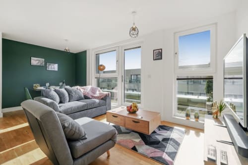 Luxury penthouse living room in Stevenage with green accent wall, striped sofa, armchair, wooden coffee table, and glass