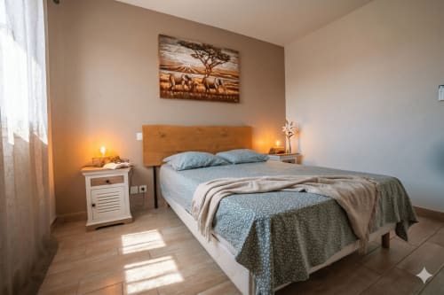 Chambre lumineuse à la villa Chez Domi avec tête de lit en bois, vue sur la piscine, éclairage chaleureux et murs beige