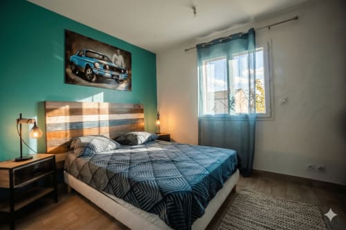 Chambre moderne à la villa Chez Domi avec mur accent turquoise, literie géométrique bleue, art automobile vintage et vue sur la piscine