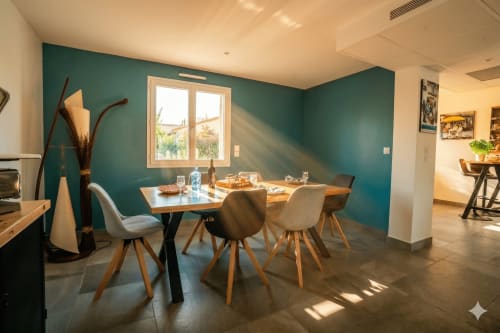 Élégante salle à manger avec mur en accent bleu-vert, table en bois et lumière naturelle à la villa Chez Domi, Canet-en-Roussillon