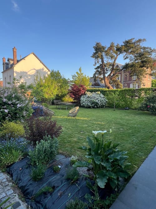 Vue ensoleillée du jardin du gîte Destination Etretat avec plantes fleuries, pelouse, sièges et bâtiments historiques, Etretat