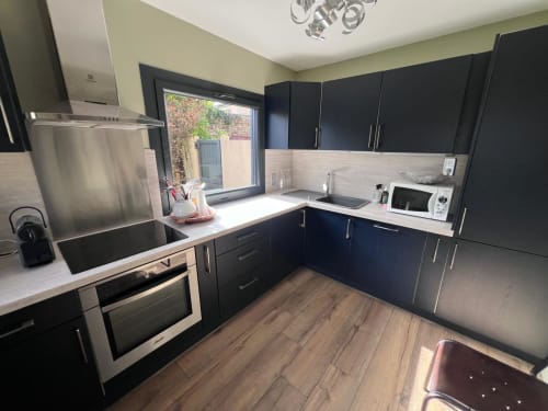 Cuisine moderne noire avec plan de travail blanc, électroménagers inox et vue sur le jardin du cottage d'Étretat