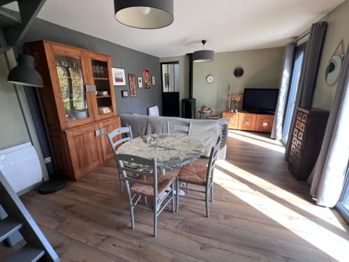 Séjour ouvert à Destination Etretat avec table en bois, cheminée en pierre, TV et vue sur le jardin