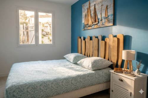Chambre lumineuse avec tête de lit en bois, mur d'accent bleu-vert, tableaux de voilier et décoration côtière à la villa Chez Mara