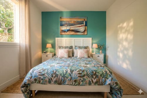Chambre côtière avec mur d'accent turquoise, tête de lit à volets blancs, literie botanique et art nautique chez Mara