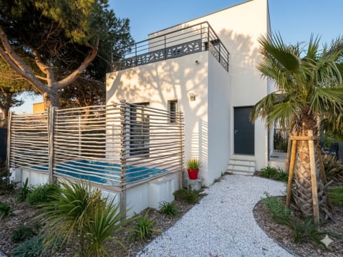 Villa blanche contemporaine à Canet-en-Roussillon avec clôture à lames horizontales, cour en graviers, palmiers et jardin méditerranéen