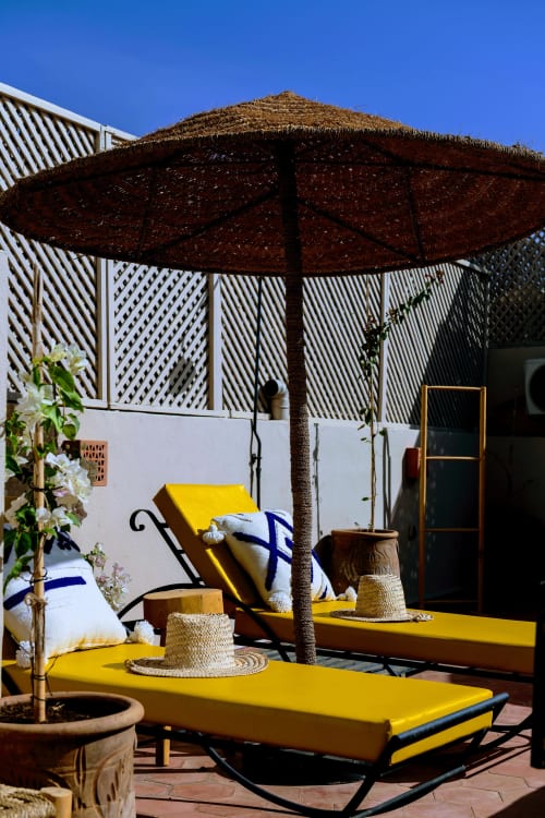 Chaises longues jaunes sous un parasol tressé à la cour du Riad Dabachi Tala'lou à Marrakech