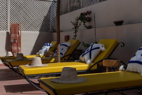 Espace détente ensoleillé au bord de la piscine du Riad Dabachi Tala'lou à Marrakech avec transats jaunes, coussins décor et palmier