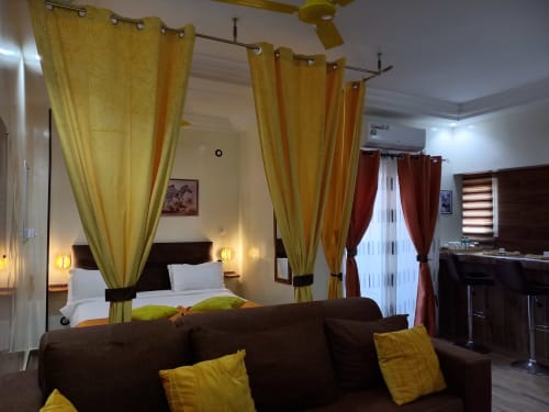Suite Junior de luxe à Zebra Résidence Bambilor avec lit à baldaquin doré, canapé marron et équipements modernes