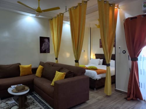 Suite junior à la Résidence Zebra à Bamilor avec canapé marron, rideaux dorés et chambre