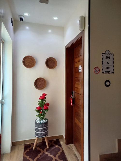 Couloir d'hôtel à la Résidence Zebra Bambilor avec paniers tissés muraux, fleurs rouges et portes de chambres en bois