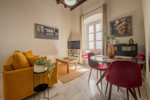 Moderno salón en Jerez Centro con sofá amarillo, sillas de comedor burdeos, mesa de cristal y vistas a la ciudad