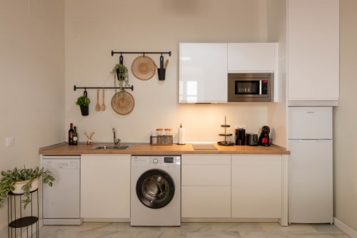 Cocina moderna con gabinetes blancos, encimera de madera, lavadora y electrodomésticos de acero inoxidable en Puerto Santa