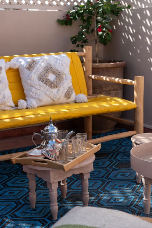 Salon jaune du Riad Dabachi Tala'lou avec coussins marocains, service à thé et plante fleurie, Marrakech