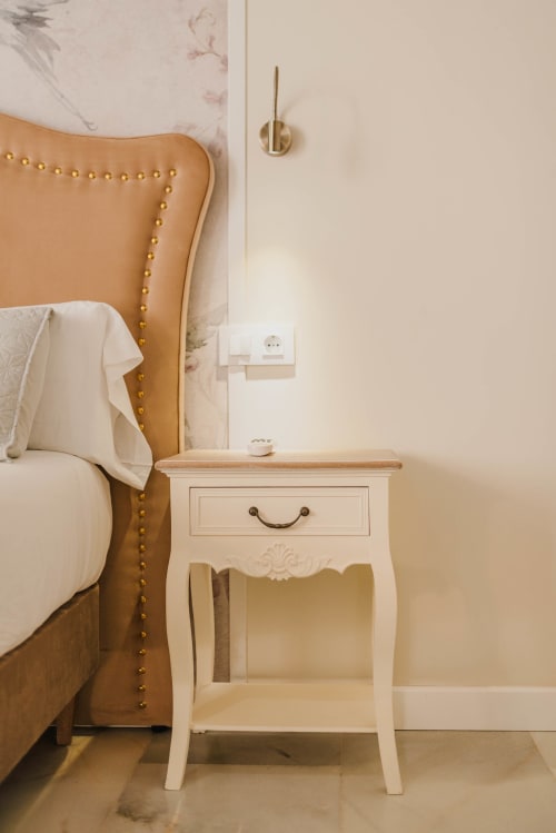Dormitorio elegante con cabecero de cuero tostado, mesilla blanca con cajón y aplique de pared en apartamento de Puerto Santa María