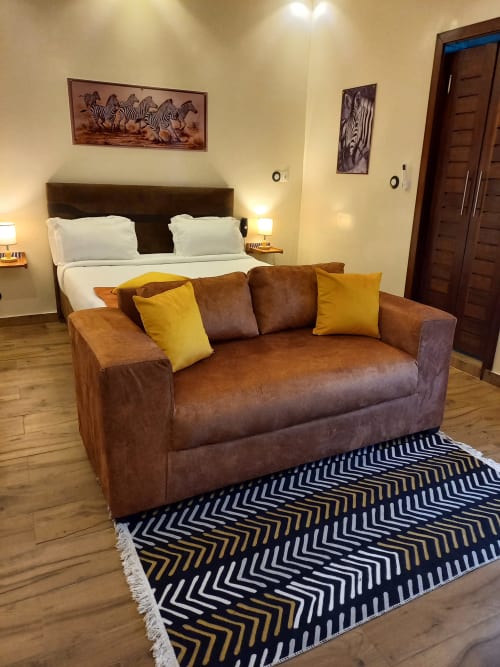 Chambre supérieure Zebra Résidence avec canapé en cuir marron, coussins jaunes, tapis rayé et lit queen-size aux draps blancs