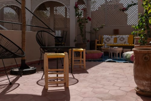Cour ensoleillée du Riad Dabachi Tala'lou à Marrakech avec chaises en bois, fauteuil Acapulco noir, carrelage en terre cuite et plantes grimpantes