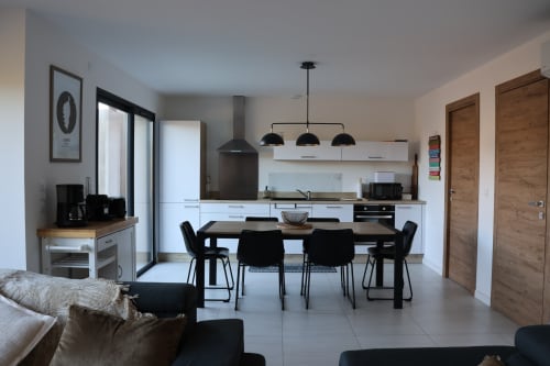 Modern open-plan kitchen and dining area in Villa Corsica with black pendant lights, white cabinetry, and dark dining table managed by the Corsu di Core