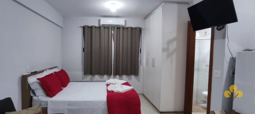 Quarto de hotel moderno no Wellington Rodovalho, Goiânia com almofadas vermelhas, guarda-roupa branco e TV na parede