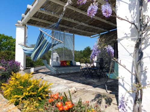 Pergolato del patio a Pietra & Luce B&B a Ostuni, con fiori viola, amaca e zona relax con vista sulla città