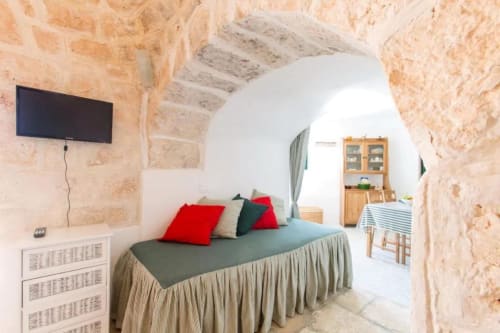 Camera Ada Trullo presso Pietra & Luce, Ostuni con muri in pietra, letto, cuscini rossi e TV