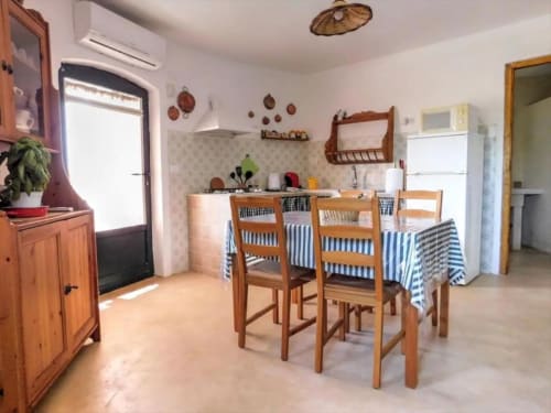 Zona cucina-pranzo rustiche dell'appartamento Ada Trullo a Pietra & Luce, Ostuni con sedie in legno, tavolo a righe blu e