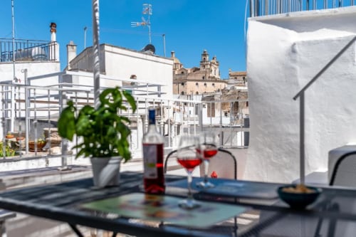 Terrazza panoramica del B&B Pietra & Luce a Ostuni con bicchieri d'aperitivo, basilico in vaso e vista sull'architettura barocca