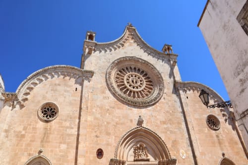 Facciata storica in pietra della chiesa di Ostuni con raffinato rosone e portale ad arco