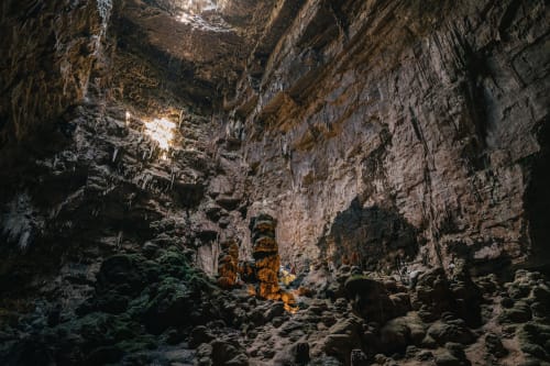 Suggestivo interno di grotta calcarea con stalattiti dorate e rocce coperte di muschio, Pietra & Luce B&B Ostuni