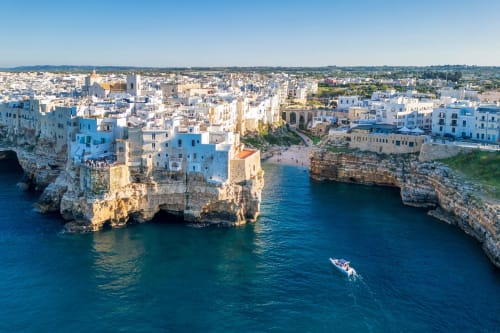 Le case imbiancate di Ostuni affacciate sulle turchesi acque adriatiche con barca, location del B&B Pietra & Luce