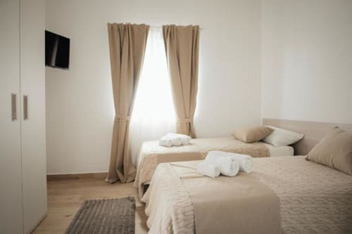 Camera Doppia Deluxe presso Casa del Sole Srl a Foggia con due letti, biancheria beige e luce naturale dalla finestra con tende