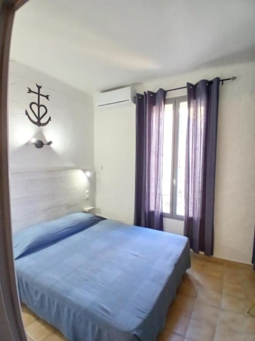 Comfortable double bedroom at Hôtel Quai d'Azur in Le Grau-du-Roi with blue bedding, purple curtains, and modern décor