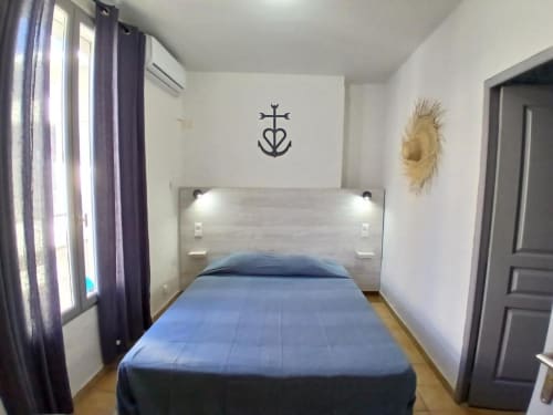 Comfortable double room at Hôtel Quai d'Azur in Le Grau-du-Roi with blue bedding, modern headboard, and decorative anchor