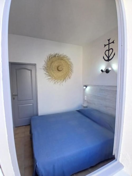 Blue double bed in bright hotel room at Hôtel Quai d'Azur, Le Grau-du-Roi with straw wall decoration