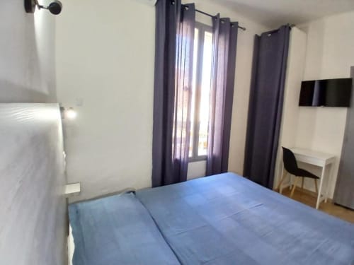 Comfortable double bedroom at Hôtel Quai d'Azur in Le Grau-du-Roi with blue bedding, desk, and purple curtains